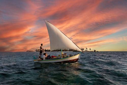 a man on a sailboat in the water at sunset at Fushifaru Maldives with 50 percent off on sea plane roundtrip 04 nights & above in Fushifaru