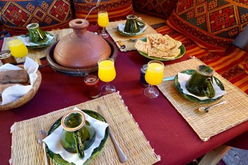 une table avec des assiettes de nourriture et des verres de jus d'orange dans l'établissement Chigaga Desert Camp, à M'Hamid El Ghizlane