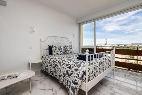 a white bedroom with a bed and a large window at T0 Vilamoura Downtown in Vilamoura