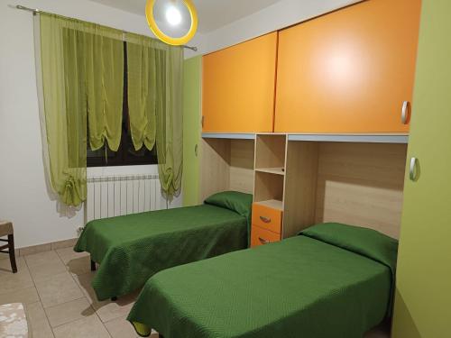 dwa łóżka w pokoju z zieloną pościelą i pomarańczowymi szafkami w obiekcie Appartamento Mary w mieście Porto Cesareo