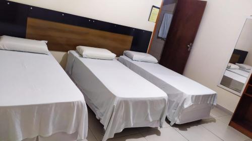 three beds in a room with white sheets at Hotel Rio Branco in Jequié
