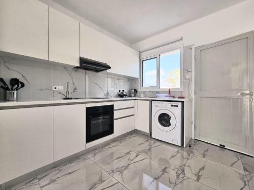 cocina con armarios blancos, lavadora y secadora en 2BD Garden Apartment, en Pafos