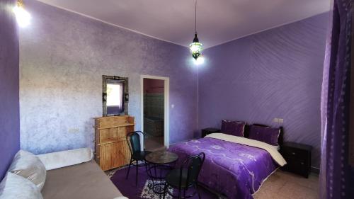 ティンジルにあるHotel camping le Soleil Tinghirの紫色のベッドルーム(ベッド1台、テーブル付)