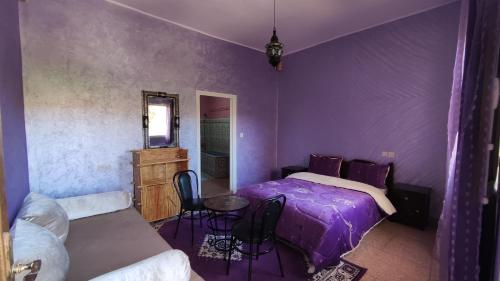 a bedroom with a purple bed and a table and chairs at Hotel camping le Soleil Tinghir in Tinerhir