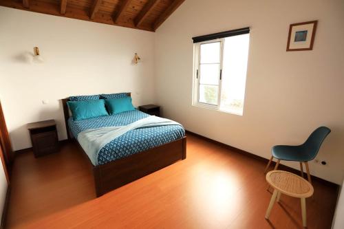 a bedroom with a bed and a chair and a window at The Blue Eden in São João