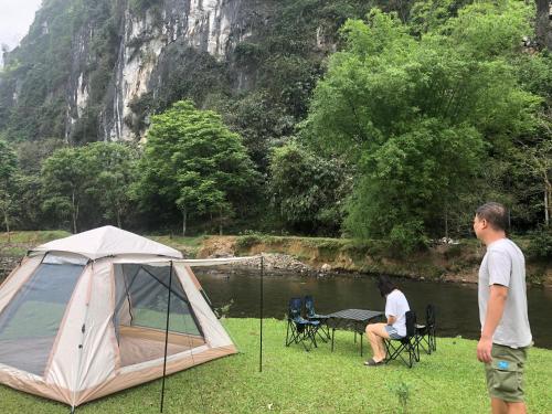Kim Bôi的住宿－Camping Suối Cái，站在湖边帐篷旁边的男人