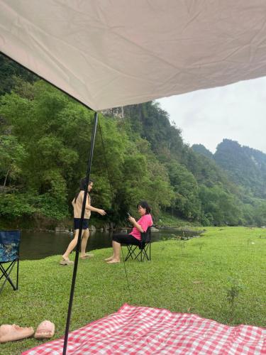 Kim Bôi的住宿－Camping Suối Cái，两个人坐在河边帐篷下的椅子上
