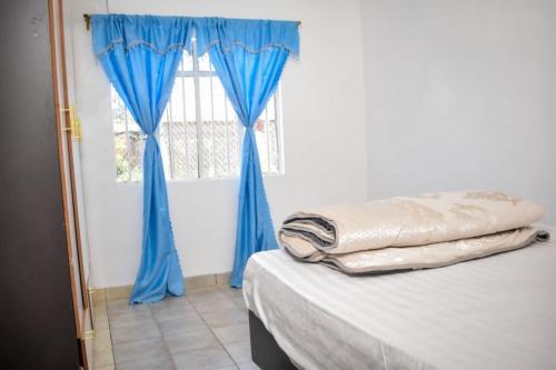 Habitación con cama con cortinas azules y ventana en Mella homes limuru, en Limuru