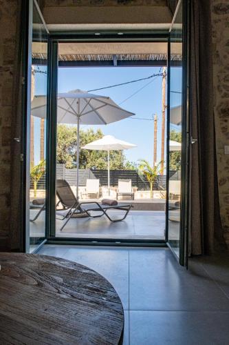 an open glass door with a table and chairs and an umbrella at Kefalas Luxury Villas Patitiri with Private Pool in Epáno Kefalás