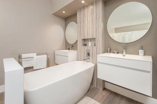 a white bathroom with a tub and a mirror at CAPE TOWN - MOUILLE POINT - SEA VIEW APARTMENT in Cape Town