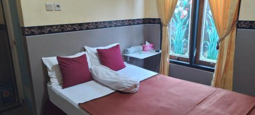 Schlafzimmer mit einem Bett mit roten Kissen und einem Fenster in der Unterkunft New KAMI Homestay in Banyuwangi