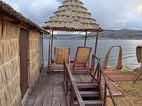 zwei Stühle und ein Regenschirm auf einem Dock neben dem Wasser in der Unterkunft CHUYPAS DEL TITICACA in Puno