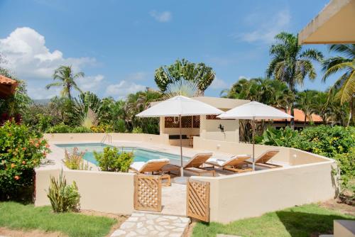 a pool with chairs and umbrellas next to a house at Villa Diana in Las Galeras