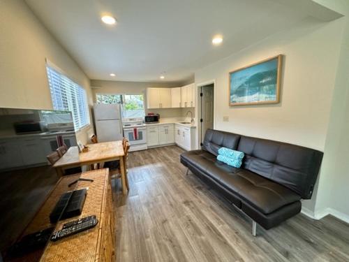 a living room with a black leather couch and a kitchen at Waimanalo Beach Cottages in Waimanalo