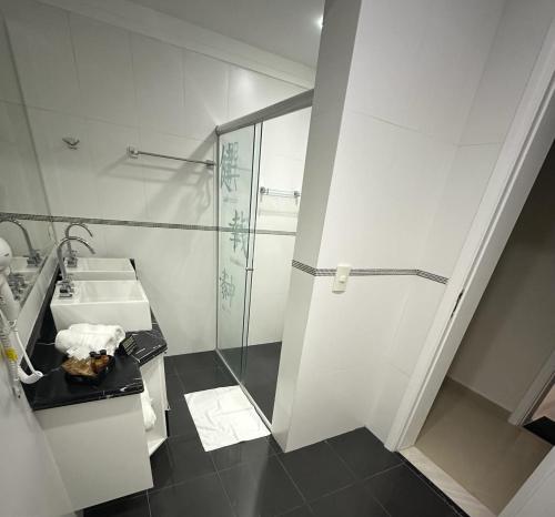 a white bathroom with a sink and a shower at Enseada Premium Suítes in Guarujá