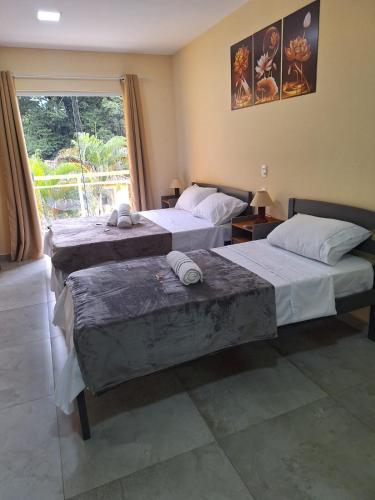 two beds in a room with a window at Suítes Recanto Petrópolis in Petrópolis