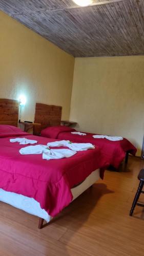 a bedroom with two beds with red sheets and white towels at Pousada Atalaia in Campos do Jordão