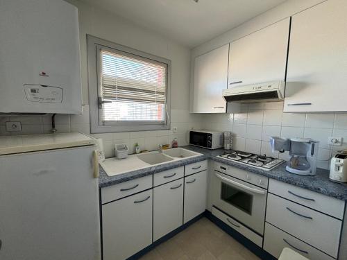 une cuisine avec des armoires blanches et un four à plaques de cuisson dans l'établissement Appartement T2 face à la plage, 4 couchages, avec balcon – Les Sables-d'Olonne - FR-1-197-534, à Les Sables-dʼOlonne