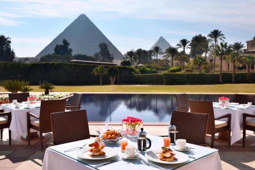 a restaurant with tables and chairs and a view of the pyramids at Marriott Mena House, Cairo in Cairo