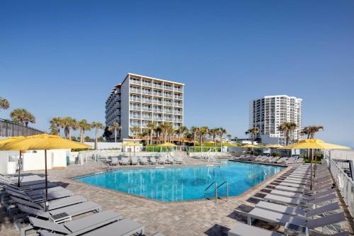 a swimming pool with lounge chairs and umbrellas at Delta Hotels by Marriott Daytona Beach Oceanfront in Daytona Beach