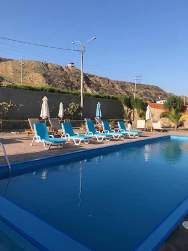 a row of chairs and umbrellas next to a swimming pool at Casuarinas del Mar Chalet Playa Caballito de Mar in Canoas De Punta Sal