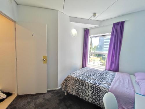 a bedroom with a bed and a window with purple curtains at City room in apartment near University in Auckland