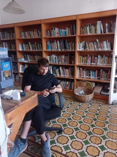 a man sitting at a desk in a library looking at his cell phone at Hostel Casa Ridgway in San José