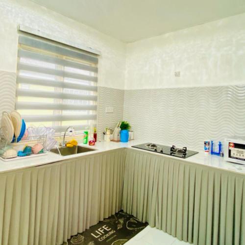 a kitchen with white counters and a sink and a window at Nuria Padang Serai Homestay in Padang Serai