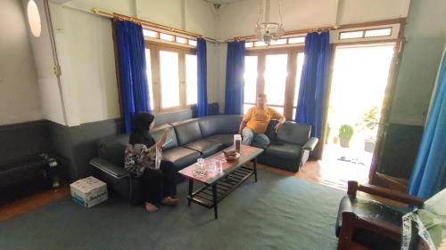 un homme et une femme assis sur un canapé dans un salon dans l'établissement Mudhahar Homestay Syariah, à Baso