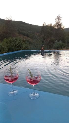 two wine glasses sitting on a table next to a swimming pool at Casa da Volta - Alentejo - S. Julião in Portalegre