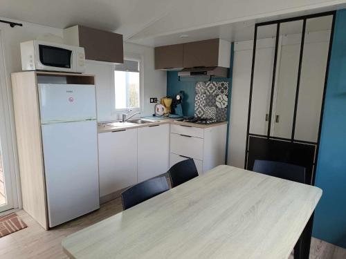 a kitchen with a table and a white refrigerator at Mobilhome Baltique in Oye-Plage