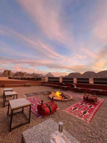 un patio avec un foyer extérieur, des tables et des montagnes dans l'établissement Wadi Rum Magic Camp, à Wadi Rum