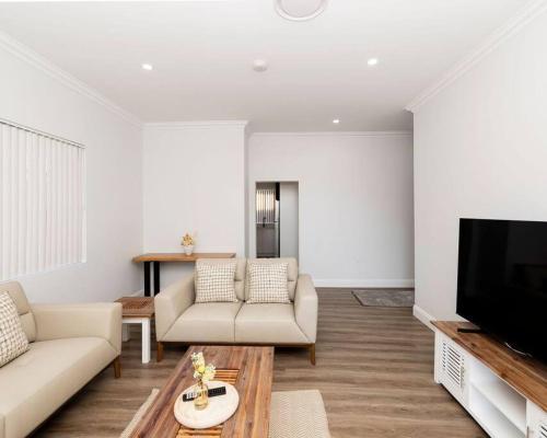 a living room with white furniture and a flat screen tv at Modern Home in the Heart of Bankstown in Bankstown