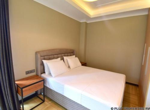 Un pequeño dormitorio con una cama blanca y una mesa en ACACUS ROYALE, en Kigali