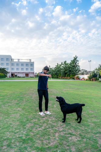 a man standing next to a black dog in a field at Playotel Resort Bhopal in Bhopal