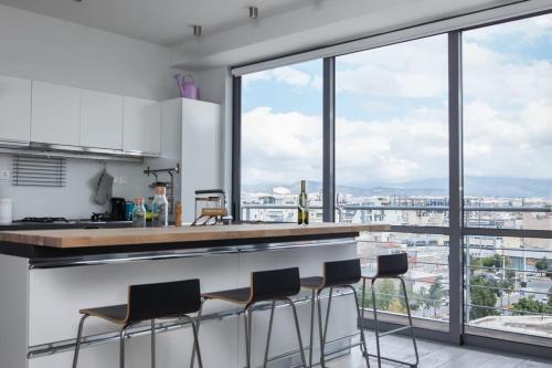 eine Küche mit einer Theke mit Hockern und großen Fenstern in der Unterkunft Penthouse with 360 View of Athens and Private Gym in Athen