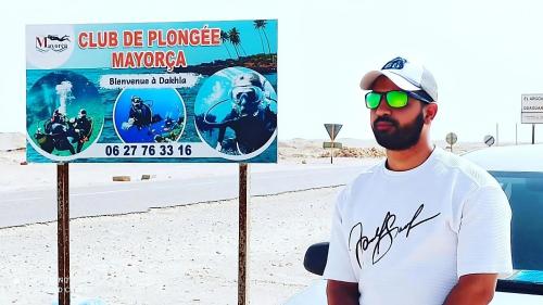 a man standing next to a sign on the beach at Mayorca scuba diving dakhla in Dakhla