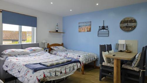 two beds in a room with blue walls and a desk at Four Winds Holiday Let in Nairn