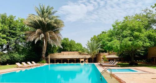 a swimming pool with lounge chairs and a palm tree at Manvār Shergarh , The Desert Resort in Dechu