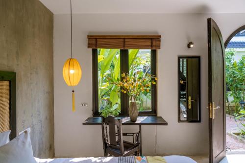 un dormitorio con una mesa y un jarrón de flores en Nghé Garden Resort Hội An, en Hoi An