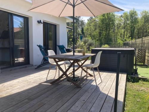 una terraza de madera con mesa y sombrilla en Superbe Studio meublé idéal pour couple ZEN avec SPA, en Sanguinet