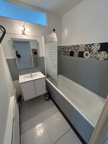 een badkamer met een wastafel, een bad en een spiegel bij Spacieux appartement avec balcon in Belfort