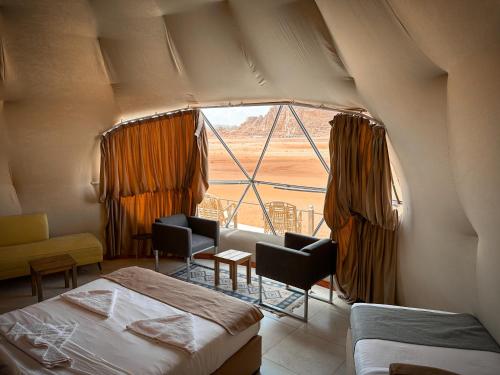 ワディ・ラムにあるRUM NEPTUNE lUXURY CAMPの砂漠の景色を望む大きな窓付きのベッドルーム1室