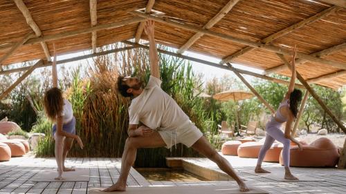 Un uomo e due ragazze che si esibiscono in una posa yoga di Moa Living a Ẕofar