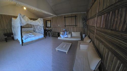 Margham的住宿－Margham Desert Safari Camp，一间设有两张床的房间和一张沙发上的女人