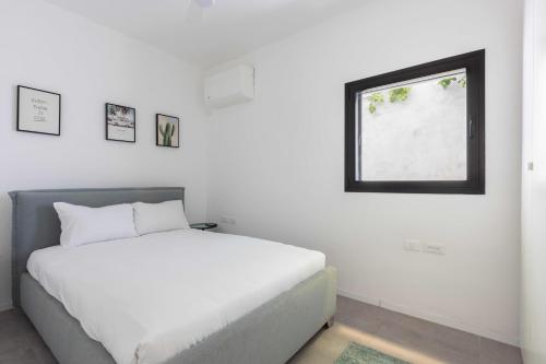 a white bedroom with a bed and a window at Eclectic Vision by TLV2RENT in Tel Aviv