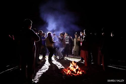 Une foule de gens debout autour d'un feu la nuit dans l'établissement Mantri Bai Camping Site Deosai, à Skardu