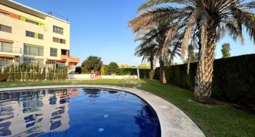 a swimming pool with a palm tree and a building at Apartamento Luna con terraza y vistas al mar in Playa Oliva Nova