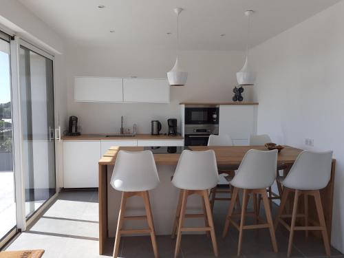 une cuisine avec une table en bois et quatre tabourets blancs dans l'établissement maison proximité mer, à Plozévet