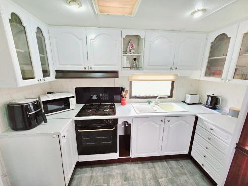 a kitchen with white cabinets and a stove top oven at Golden Anchor 8b9 Caravan Park Holiday Home in Chapel Saint Leonards